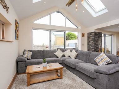 A living room with a grey L-shaped sofa a wooden coffee table and large windows at The Herun in Rhosneigr