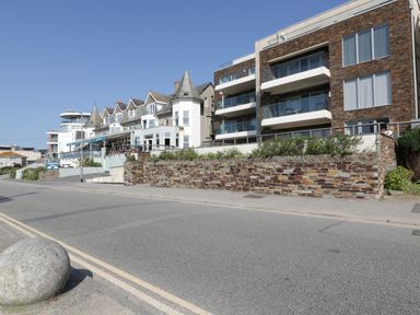A street view of a row of buildings including modern apartments and older houses with stone walls at Newquay Fistral Beach View in Newquay