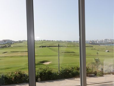 A view of a golf course with bunkers and green fields seen through a large glass window at Newquay Fistral Beach View in Newquay