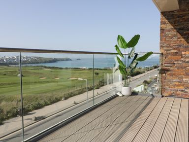 A balcony with a potted plant and glass railing overlooking a golf course and coastline at Newquay Fistral Beach View in Newquay