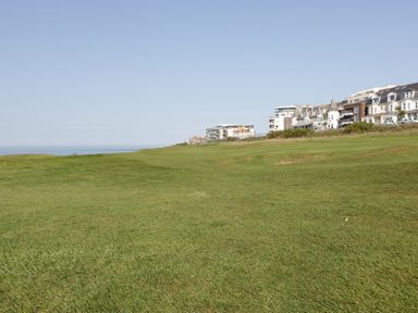 A grassy open field with buildings along the edge under a clear sky at Newquay Fistral Beach View in Newquay