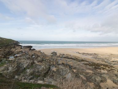 A rocky coastline with a sandy beach and ocean waves under a cloudy sky at Newquay Fistral Beach View in Newquay