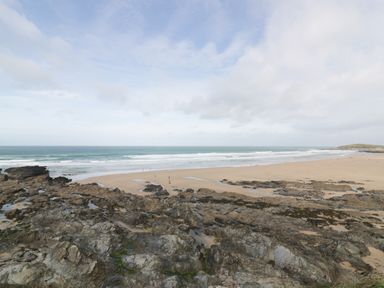 A beach with rocky foreground waves and people walking at Newquay Fistral Beach View in Newquay