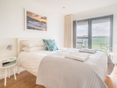 A bedroom with a bed and blue pillows next to a sliding glass door with a view at Newquay Fistral Beach View in Newquay