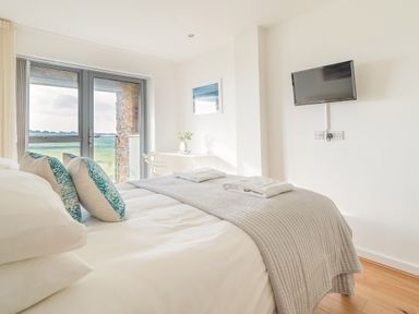 A bedroom with a bed pillows a wall mounted television and a balcony door at Newquay Fistral Beach View in Newquay