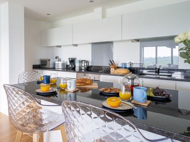 A modern kitchen with a black countertop island set for breakfast with orange juice croissants and coffee at Newquay Fistral Beach View in Newquay
