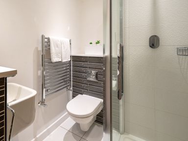 A bathroom with a wall-mounted toilet, a heated towel rail, a small sink, and a glass shower enclosure at Newquay Fistral Beach View in Newquay