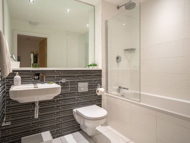 A bathroom with a wall-mounted sink and toilet a bathtub with a glass shower screen and a large mirror above the sink at Newquay Fistral Beach View in Newquay
