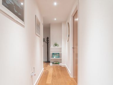 A hallway with wooden floor a white shelf with plants books and a framed picture and a wooden door at Newquay Fistral Beach View in Newquay