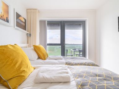 A bedroom with two beds yellow pillows and a balcony with a table and chairs at Newquay Fistral Beach View in Newquay