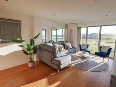 A living room with a gray sofa, two blue chairs, a coffee table, a floor lamp, a large mirror, and a plant at Newquay Fistral Beach View in Newquay