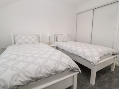 A bedroom with two single beds with patterned bedding a bedside table with a lamp and a sliding door closet at Amble Views in Amble