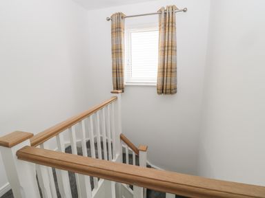 A stairwell with wooden handrails white balusters and a window with plaid curtains at Amble Views in Amble