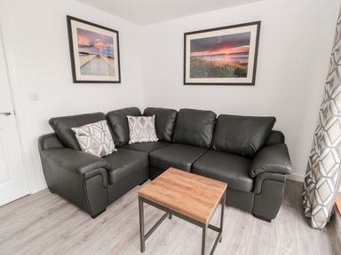 A corner sofa with two patterned cushions a wooden coffee table and framed pictures on the wall at Amble Views in Amble