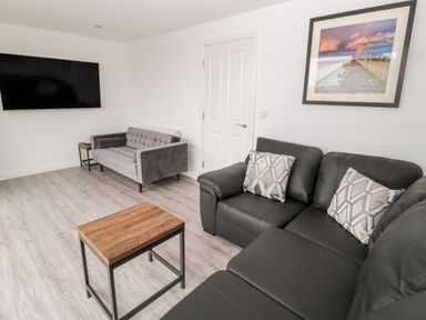 A living room with a black sofa with pillows a grey loveseat a wooden coffee table a wall-mounted TV and a framed picture at Amble Views in Amble