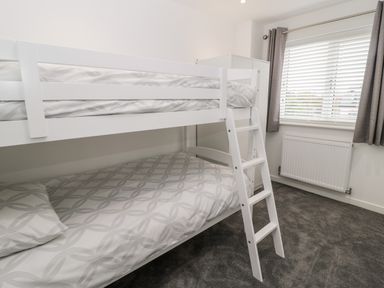 A bedroom with a white bunk bed next to a window with gray curtains and a radiator at Amble Views in Amble