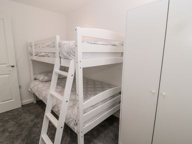 A bedroom with a white bunk bed with patterned bedding and a white wardrobe at Amble Views in Amble