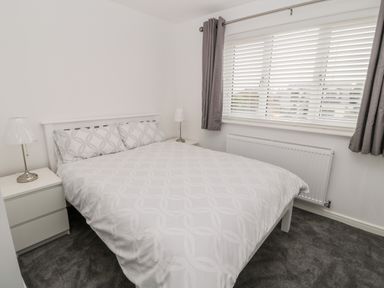 A bedroom with a double bed between two bedside tables with lamps and a window with blinds and curtains at Amble Views in Amble