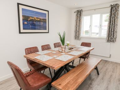 A dining room with a wooden table surrounded by brown chairs and a wooden bench at Amble Views in Amble