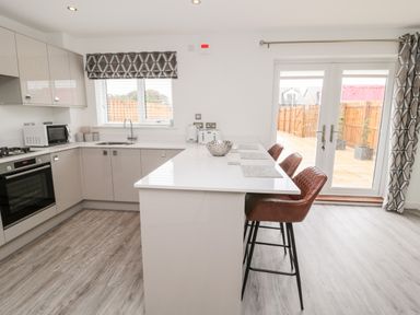 A modern kitchen with a white countertop island and brown bar stools at Amble Views in Amble
