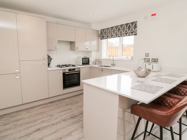 A kitchen with beige cabinets a white countertop brown bar stools a window with blinds and various kitchen appliances at Amble Views in Amble