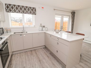 A kitchen with a sink, countertop, built-in oven, toaster, kettle, and bar stools at Amble Views in Amble