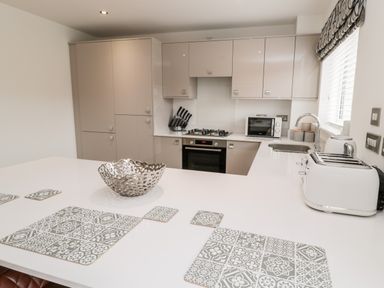 A kitchen with beige cabinets white countertop a gas stove microwave toaster and patterned placemats at Amble Views in Amble