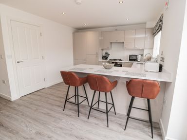 A kitchen with three brown chairs at a white counter and built-in appliances at Amble Views in Amble