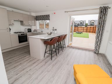 A kitchen with an island, three bar stools, a gas stove, microwave, and chairs next to an open door leading to a fenced backyard at Amble Views in Amble