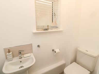 A small bathroom with a sink, toilet, and window with decorative items on the windowsill at Amble Views in Amble