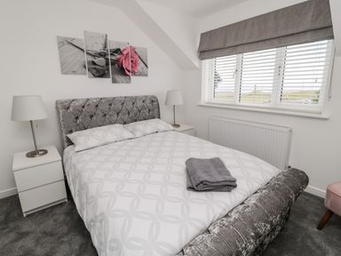 A bedroom with a bed a grey headboard grey blankets bedside tables with lamps and a window with blinds at Amble Views in Amble