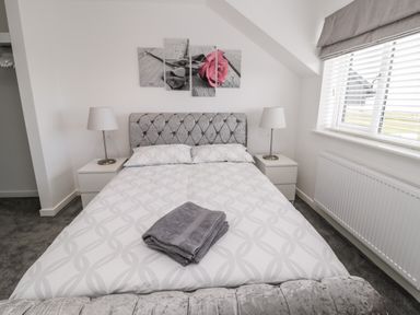 A bedroom with a bed with folded towels on it two bedside tables with lamps and a window with blinds at Amble Views in Amble