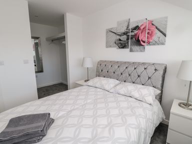 A bedroom with a bed with patterned white bedding two bedside lamps a mirror and a wall art of a pink rose at Amble Views in Amble