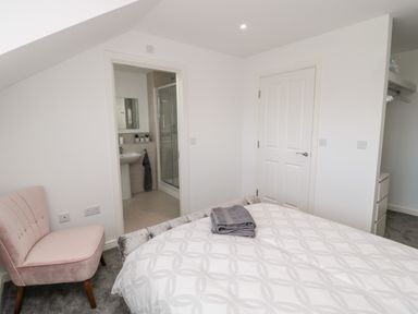 A bedroom with a bed, a pink chair, a door leading to a bathroom, and a closet at Amble Views in Amble
