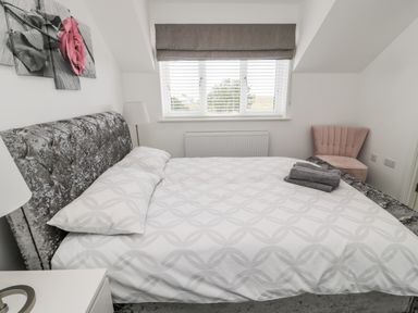 A bedroom with a bed a bedside lamp a pink chair and window at Amble Views in Amble