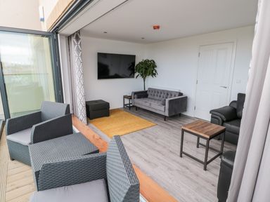 A living room with a gray sofa black armchairs yellow rug and outdoor seating area at Amble Views in Amble