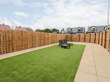 A fenced backyard with artificial grass two black lounge chairs and tiled pathways at Amble Views in Amble