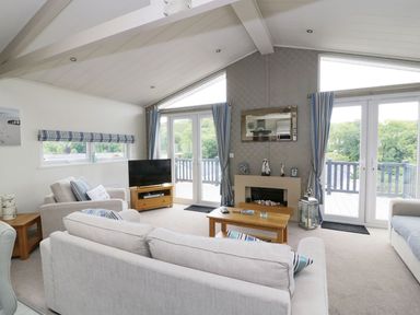 A living room with sofas a coffee table a television and glass doors opening to a balcony at 44 Heritage Park Stepaside near Kilgetty