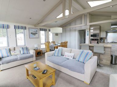 A living room with two sofas a wooden coffee table dining table with chairs and a kitchen with bar stools at 44 Heritage Park in Stepaside near Kilgetty