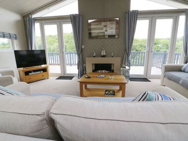 A living room with sofas a coffee table a television and glass doors opening to a balcony at 44 Heritage Park Stepaside near Kilgetty