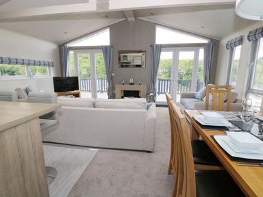 An open plan living room with sofas a dining table and chairs a TV and windows with curtains at 44 Heritage Park Stepaside near Kilgetty