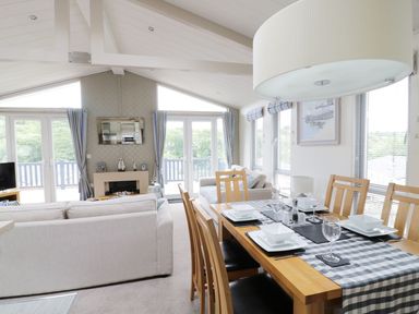 A dining table set for four with plates and glasses next to a living area with sofas and a fireplace at 44 Heritage Park in Stepaside near Kilgetty
