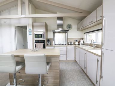 A kitchen with a wooden island and two white stools a stove microwave toaster and sink at 44 Heritage Park Stepaside near Kilgetty