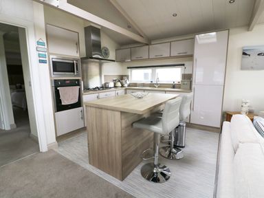 A kitchen with a wooden island and two chairs next to a living area at 44 Heritage Park in Stepaside near Kilgetty
