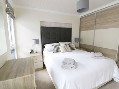 A bedroom with a bed and folded towels on it two bedside tables with lamps and a wooden wardrobe at 44 Heritage Park in Stepaside near Kilgetty