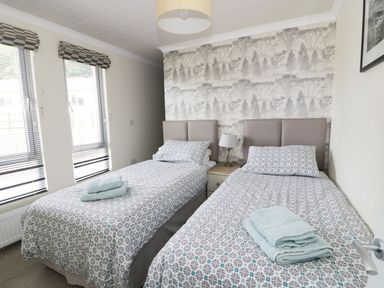 A bedroom with two single beds a bedside table and lamp at 44 Heritage Park Stepaside near Kilgetty