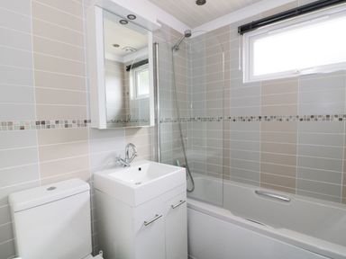A bathroom with a toilet a sink cabinet a mirror a bathtub with a shower and a window at 44 Heritage Park Stepaside near Kilgetty
