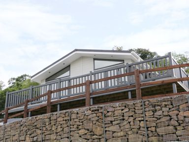 A white house with triangular windows and a wooden deck behind a stone retaining wall at 44 Heritage Park in Stepaside near Kilgetty