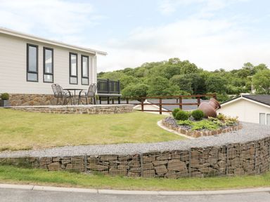 A patio with chairs and table outside a house with stone wall and garden at 44 Heritage Park Stepside near Kilgetty