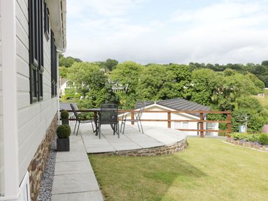 A patio with a table and chairs next to a white house with a stone base surrounded by grass at 44 Heritage Park Stepaside near Kilgetty